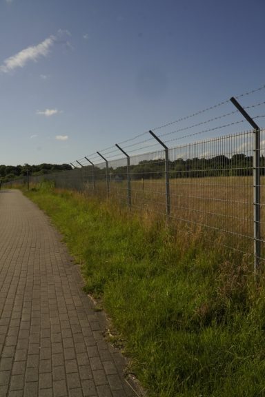 Weitläufiger Weg entlang eines Maschendrahtzauns bei Klarem Himmel