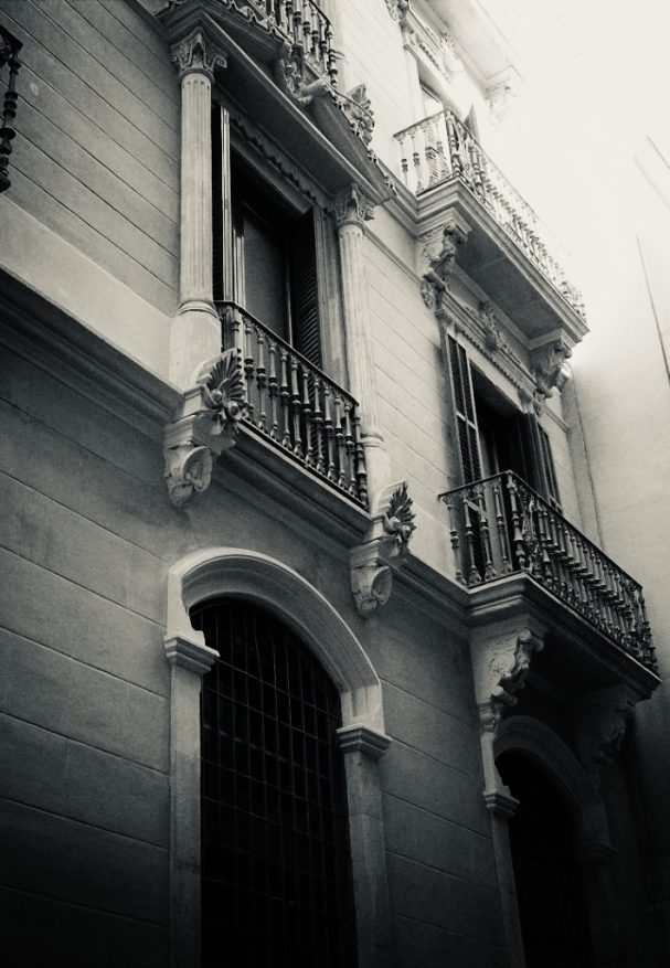 "Schwarzweißfoto einer historischen Hausfassade mit Balkone in Barcelona in Licht-Schattenspiel.