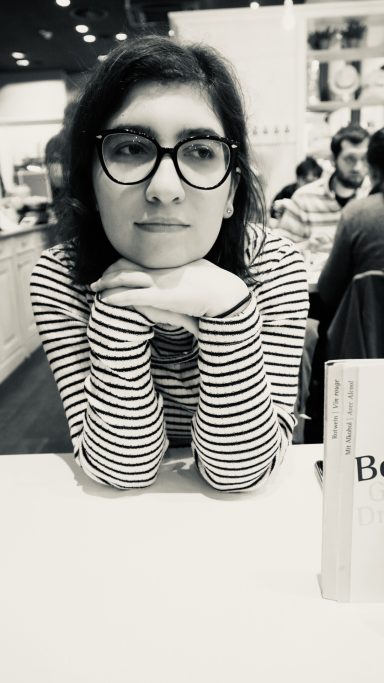 Frau mit Brille stützt das Kinn auf die Hände und schaut  nachdenklich ins Leere. Schwarzweißaufnahme im Café
